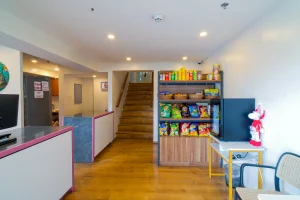 MySpace hotel comembo lobby with wooden floors, a snack display shelf filled with chips and instant noodles, and a reception counter.