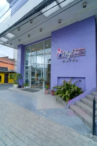 Exterior view of MySpace Comembo with a purple facade, glass entrance, and potted plants near the doorway.