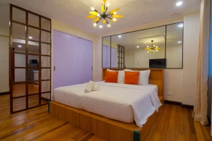 Spacious room with a large bed, orange accent pillows, and warm lighting reflected on a wall mirror.